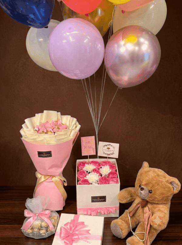 Luxury gift set featuring a brown teddy bear, chocolate bouquet, birthday roses in a box, and colorful balloons against a dark brown background.