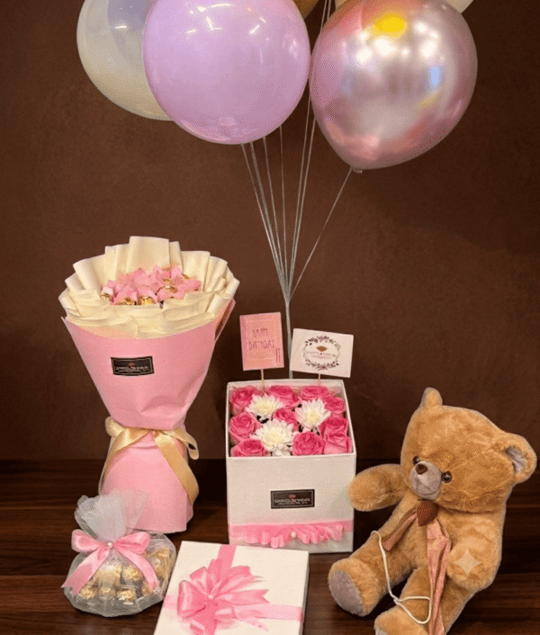 Luxury gift set featuring a brown teddy bear, chocolate bouquet, birthday roses in a box, and colorful balloons against a dark brown background.