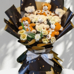 A detailed view of a deluxe Teddy Bear Bouquet Lahore, featuring six cuddly plush bears (brown and beige) and elegant artificial white roses, expertly arranged in premium black wrapping with gold patterns and a large white satin ribbon, resting on a white display pedestal.