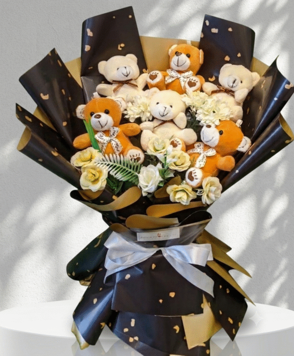A detailed view of a deluxe Teddy Bear Bouquet Lahore, featuring six cuddly plush bears (brown and beige) and elegant artificial white roses, expertly arranged in premium black wrapping with gold patterns and a large white satin ribbon, resting on a white display pedestal.